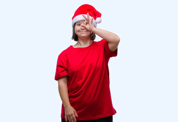 唐氏综合症的年轻成年妇女戴着圣诞帽在孤立的背景下做 手势用手微笑 眼睛看通过手指与愉快的面孔 — 图库照片