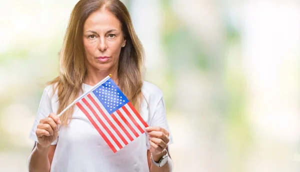 Middle age hispanic woman holding flag of United States of America over isolated background with a confident expression on smart face thinking serious