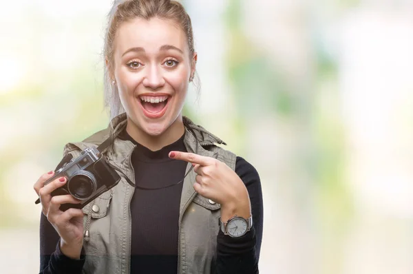 年轻的金发女子拍摄图片使用老式相机在孤立的背景非常高兴地指着手和手指 — 图库照片