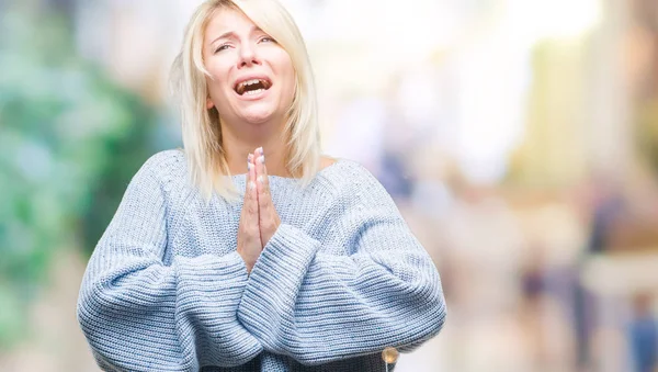 Young beautiful blonde woman wearing winter sweater over isolated background begging and praying with hands together with hope expression on face very emotional and worried. Asking for forgiveness. Religion concept.