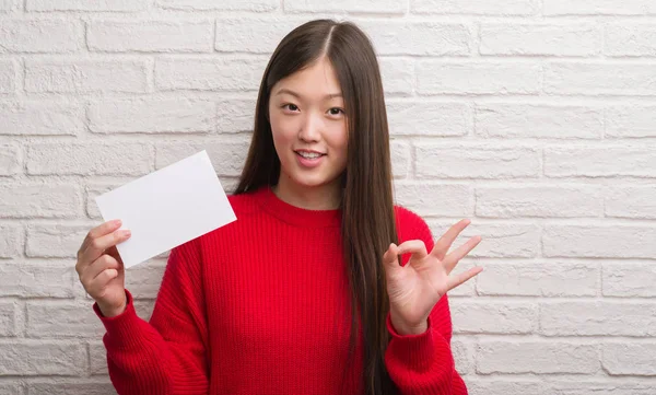 年轻的中国妇女在砖墙上举行空白纸做 符号与手指 优秀的符号 — 图库照片