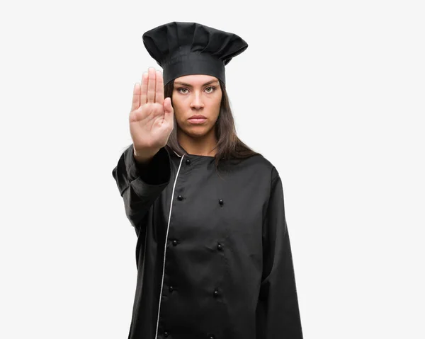 年轻的西班牙裔厨师妇女穿着厨师制服与张开手做停止标志认真和自信的表达 防守姿态 — 图库照片