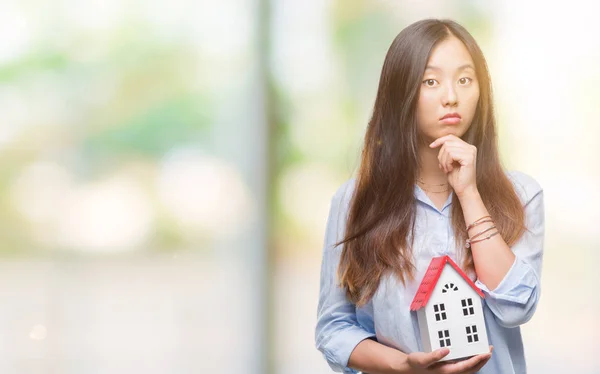 Young asian woman real state agent holding house isolated background serious face thinking about question, very confused idea