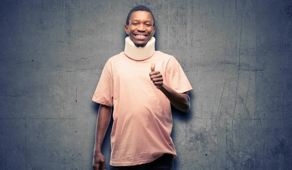 Injured african black man wearing neck brace smiling broadly showing thumbs up gesture to camera, expression of like and approval