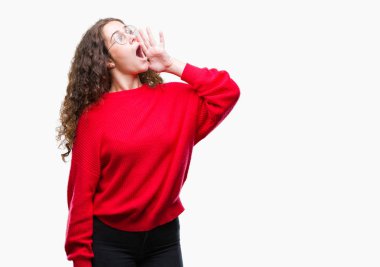 Güzel esmer kıvırcık saçlı Genç kız bağırarak ve ağzı üzerinde el ile yan için çığlık izole arka plan üzerinde gözlük ve kış kazak giyiyor. İletişim kavramı.