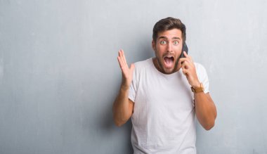 Yakışıklı genç gri grunge üzerinde duvar büyük gülümseme ile çığlık zaferini kutluyor ve ellerini kaldırdı telefon çok mutlu ve heyecanlı, kazanan ifade üzerinde konuşma