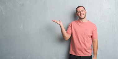 Neşeli sunulması ve kameraya bakarak avucunun ile işaret gülümseyen gri grunge duvarın üzerinden beyaz delikanlı.