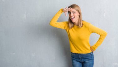 Grunge gri duvardan çok mutlu ve gülümseyen uzakta el ile üzerine kafa seyir duran güzel genç kadın. Arama kavramı.