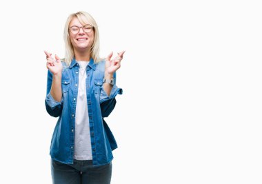 Umut ve gözleri kapalı geçiş parmaklarıyla gülümseyen izole arka plan üzerinde gözlük takan genç güzel sarışın kadın. Şans ve batıl kavramı.