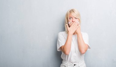 Yetişkin beyaz kadın grunge gri duvar eller için hata ile ağız kapsayan şok yüzünden. Gizli kavramı.