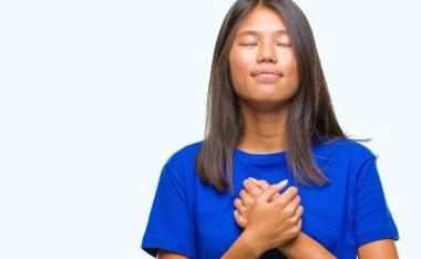 Genç Asyalı kadın ile gülümseyen izole arka plan üzerinde kapalı gözler ve yüzünde minnettar jest ile göğüs üzerinde eller. Sağlık kavramı.