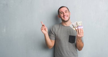 Bir tomar para çok mutlu el ve parmak ile tarafına işaret tutan gri grunge duvarın üzerinden beyaz delikanlı