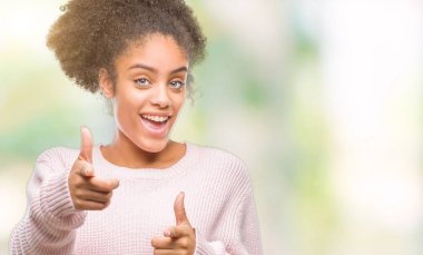 Fotoğraf makinesi ile mutlu ve komik yüz için parmakları işaret izole arka plan üzerinde kış kazak giyen genç afro Amerikalı kadın. İyi enerji ve vibes.