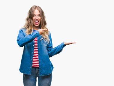 Hayret ve el ile sunulması ve parmak ile işaret ederken kameraya gülümseyen izole arka plan üzerinde sarışın güzel genç kadın.