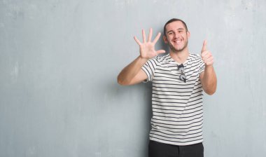 Beyaz delikanlı gösterilen ve parmakları ile işaret gri grunge duvarın üzerinden 6 kendinden emin ve mutlu gülümseyerek iken numara.