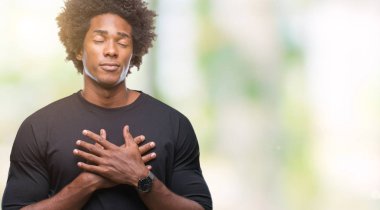 Afro Amerikalı adam ile gülümseyen izole arka plan üzerinde kapalı gözler ve yüzünde minnettar jest ile göğüs üzerinde eller. Sağlık kavramı.