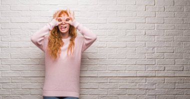 Dilini, parmaklarının arasından baktığını yapışmasını dürbün gibi ok jest yapıyor tuğla duvarın üzerinden duran genç Kızıl saçlı kadın. Deli ifade.