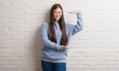 Beyaz tuğla duvar eller eller büyük gösterilen ve büyük boy işareti, ölçü birimi sembolü ile üzerinde genç Chinise kadın. Kameraya bakarak gülümsüyordu. Ölçüm kavramı.