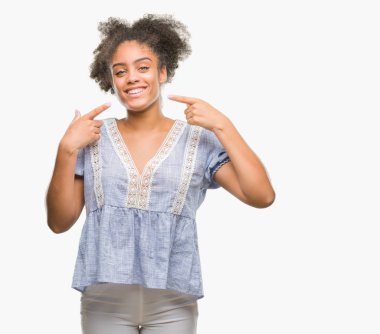 Kendinden emin gösterilen ve işaret parmakları diş ve ağız ile gülümseyen izole arka plan üzerinde genç afro Amerikalı kadın. Sağlık kavramı.