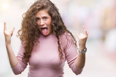 Deli ifade rock simge elle yapıyor ile bağırarak arka plan üzerinde pembe kazak giyen genç kız izole güzel esmer kıvırcık saçlı. Müzik yıldızı. Ağır kavramı.