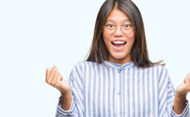 Genç Asyalı kadın kutluyor izole arka plan üzerinde şaşırttı ve başarı için kaldırdı kollarını açarak hayret ve gözleri açık. Kazanan kavramı.