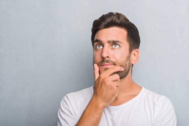 Yakışıklı genç gri grunge duvar ciddi bir yüz düşünme hakkında soru, çok karışık bir fikir üzerinde