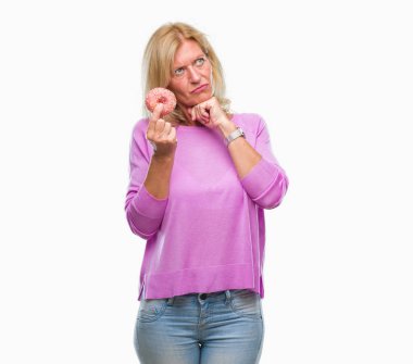 Orta yaş sarışın kadın izole arka plan ciddi bir yüz düşünme hakkında soru, çok karışık bir fikir üzerinde pembe çörek yeme