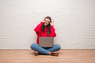 Mutlu yüz el parmaklarının arasından seyir göz üzerinde ok işaretiyle yapıyor gülümseyen ile dizüstü bilgisayar kullanarak beyaz tuğla duvarın üzerinden katta oturan genç esmer kadın