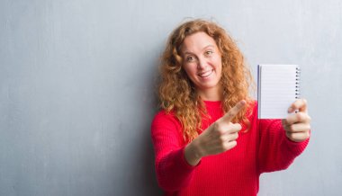 Gri grunge duvar gösteren boş dizüstü el ve parmak ile işaret çok mutlu genç Kızıl saçlı kadın