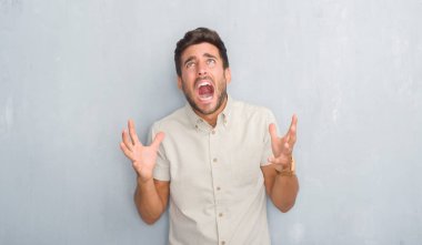 Yakışıklı genç gri grunge üzerinde duvar giyen Yaz gömlek çılgın ve kızgın bağırarak ve agresif ifade ve silah kaldırdı bağırıyordu. Hayal kırıklığı kavramı.