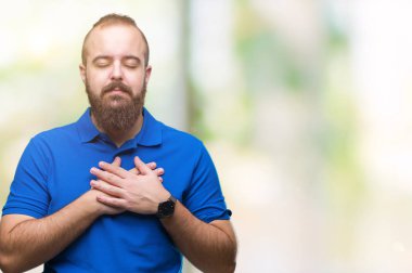 Genç beyaz hipster adam kapalı gözler ile göğüs ellerinde ve yüzünde minnettar jest ile gülümseyen izole arka plan üzerinde mavi tişört giyiyor. Sağlık kavramı.