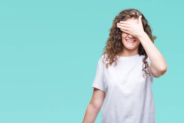 Güzel esmer kıvırcık saçlı Genç kız gülümsüyor ve gözleri için sürpriz kapsayan yüz el ile gülüyor izole arka plan üzerinde rahat t-shirt giyiyor. Kör kavramı.
