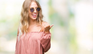 Güzel genç sarışın kadın arıyorum ve başparmak yanında yukarıyı mutlu yüz ile gülümseyen izole arka plan üzerinde Retro güneş gözlüğü takıyor.