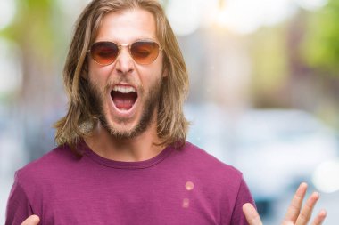 Genç yakışıklı adam uzun saçlı deli ve çığlık kaldırdı ve kapalı gözleri heyecanlı silah ile başarı için deli kutluyor izole arka plan üzerinde güneş gözlüğü takıyor. Kazanan kavramı