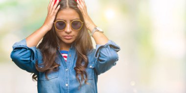 Genç güzel Arap kadın güneş gözlüğü takmış çünkü umutsuz ve stresli baş ağrısı acı izole arka plan üzerinde ağrı ve migren. Ellerini kafasına.