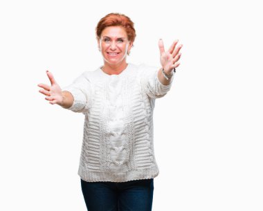 Sarılmak için kollarını açarak gülümseyerek kameraya bakarak izole arka plan üzerinde kış kazak giyen Atrractive üst düzey beyaz Kızıl saçlı kadın. Neşeli ifade kucaklayan mutluluk.