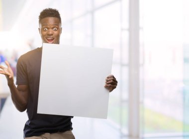 Kocaman bir gülümseme ile çığlık ve ellerini kaldırdı zaferini kutluyor bir afiş çok mutlu ve heyecanlı, kazanan ifade tutan genç Afro-Amerikan adam