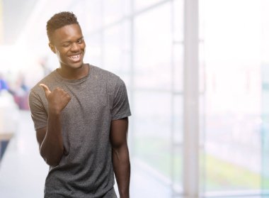 Gri t-shirt arıyorsunuz ve başparmak yanında yukarıyı mutlu yüz ile gülümseyen giyen genç Afro-Amerikan adam.