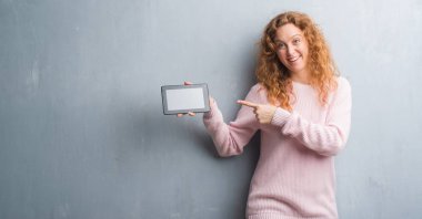 El ve parmak ile işaret çok mutlu tablet kullanarak gri grunge duvar genç Kızıl saçlı kadın