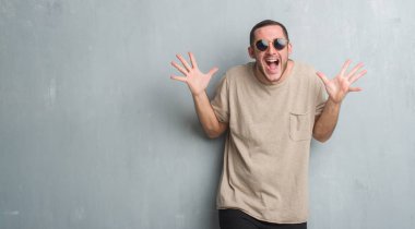 Gri grunge üzerinde beyaz delikanlı duvar giyen güneş gözlüğü deli ve çığlık kaldırdı ve açık gözleri heyecanlı silah ile başarı için hayran kutluyor. Kazanan kavramı