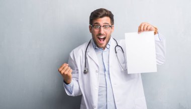 Yakışıklı genç doktor adam gurur çığlık ve zafer ve başarı çok heyecanlı, kutluyor gri grunge duvar holding sayfa boş sözleşme duygu tezahürat