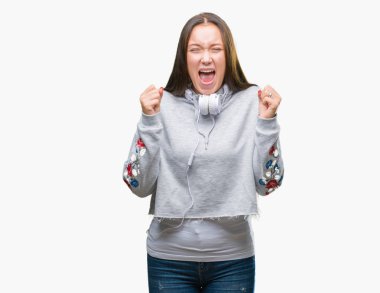 Üzerinde kulaklık giyen genç güzel beyaz öğrenci kadın deli kutluyor arka plan izole ve çığlık kaldırdı ve açık gözleri heyecanlı silah ile başarı için hayrete düşürdü. Kazanan kavramı