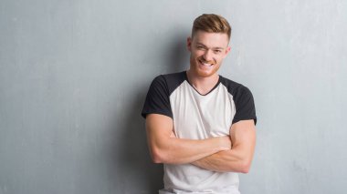 Üzerinde gri grunge Duvar ile mutlu yüz gülümseyen genç Kızıl saçlı adam kameraya seyir silah geçti. Olumlu bir kişi.