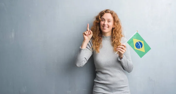 Young Redhead Woman Grey Grunge Wall Holding Flag Brazil Surprised — Stock Photo, Image