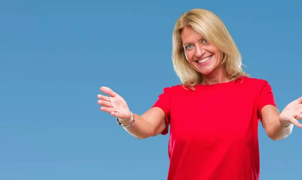 Middle age blonde woman over isolated background looking at the camera smiling with open arms for hug. Cheerful expression embracing happiness.