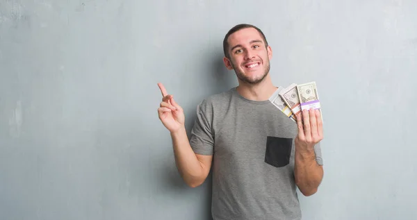灰色のグランジ壁側の手と指で指す非常に幸せなお金の束を持って若い白人男 — ストック写真