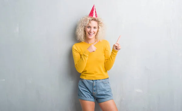 Jovem Loira Sobre Grunge Parede Cinza Usando Chapéu Aniversário Sorrindo — Fotografia de Stock