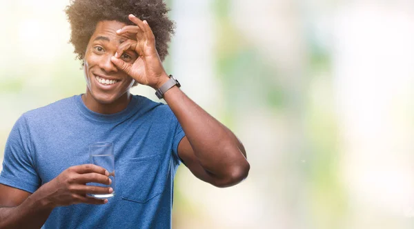 Afro american man drinking glass of water over isolated background with happy face smiling doing ok sign with hand on eye looking through fingers