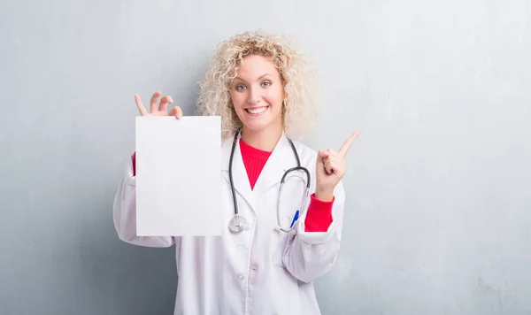 Junge Blonde Ärztin Über Grunge Graue Wand Mit Leerem Papierbogen — Stockfoto