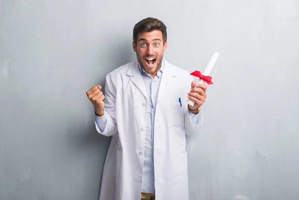Handsome Young Doctor Man Grey Grunge Wall Holding Diploma Screaming — Stock Photo, Image